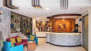 A hotel reception area with a wooden reception desk, a large elephant mural, and colorful seating. - The Monarch Hotel (Nairobi)