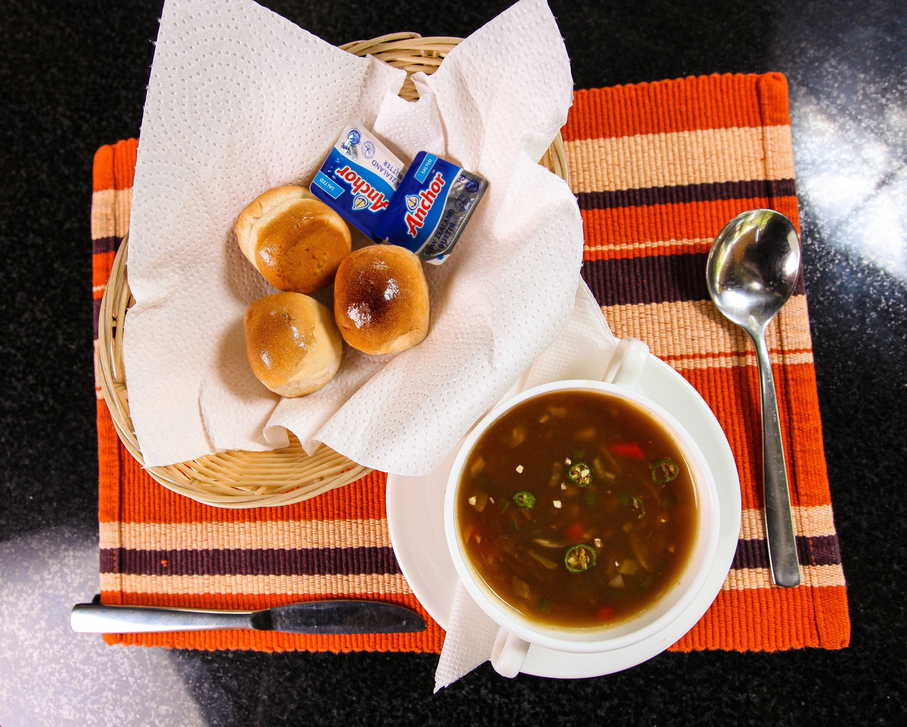 A meal with soup and rolls on a striped placemat.