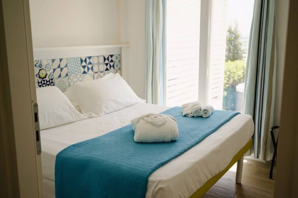 A hotel room with a bed, a blue blanket, and rolled towels.