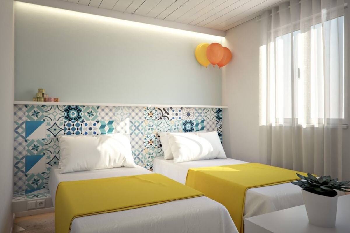 A hotel room with two beds, a patterned headboard, and a window with curtains.
