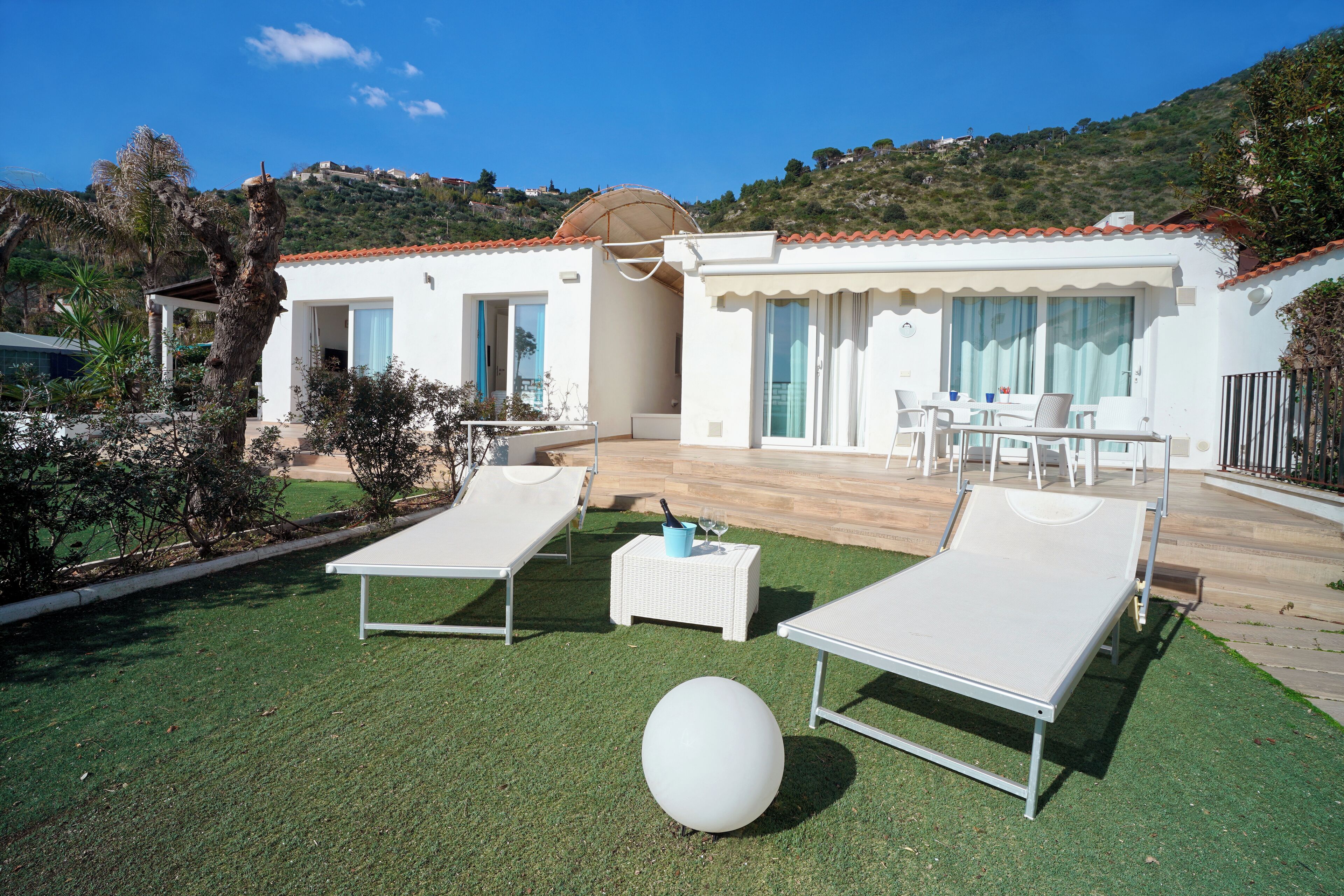 A villa with a patio area featuring two lounge chairs, a small table, and a white spherical object.