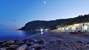 Une plage avec un rivage rocheux, une mer calme et un bâtiment illuminé sur la droite.