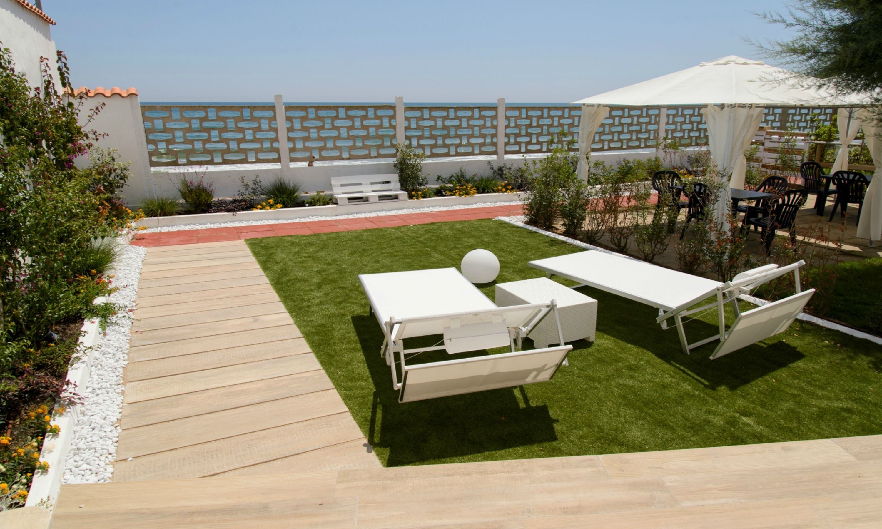 Um pátio com duas espreguiçadeiras brancas, um guarda-sol branco e um deck de madeira.