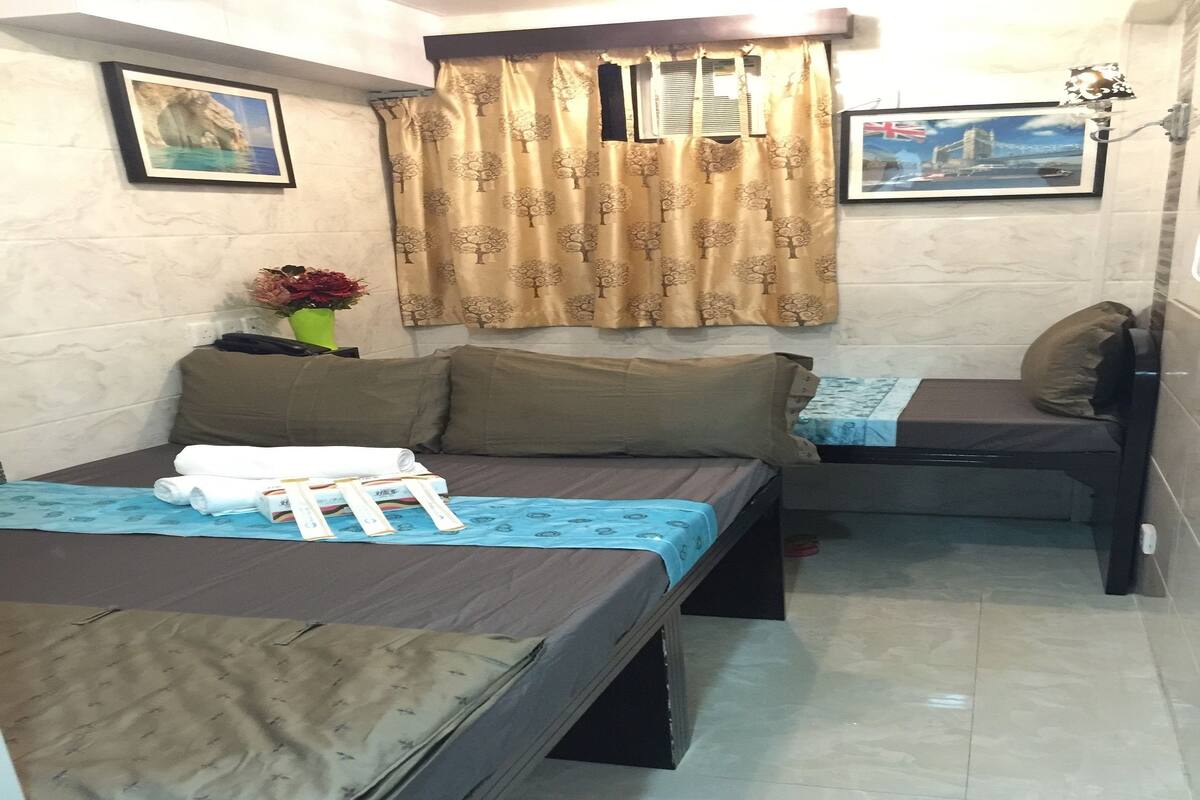 A room with two beds, a small table with a vase of flowers, and two framed pictures on the walls.