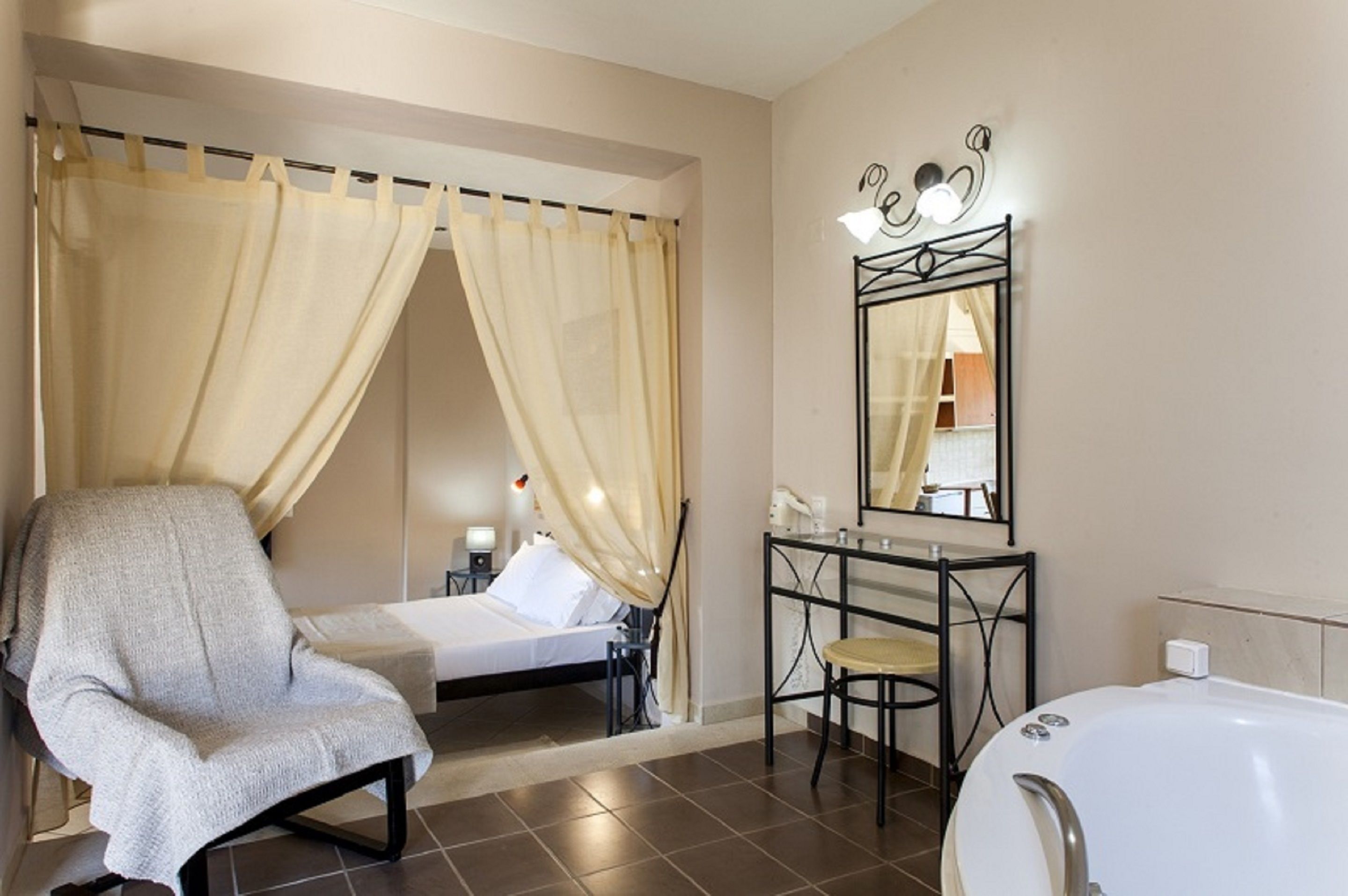 Een hotelkamer met een bed, een stoel, een kaptafel met spiegel en een bad.