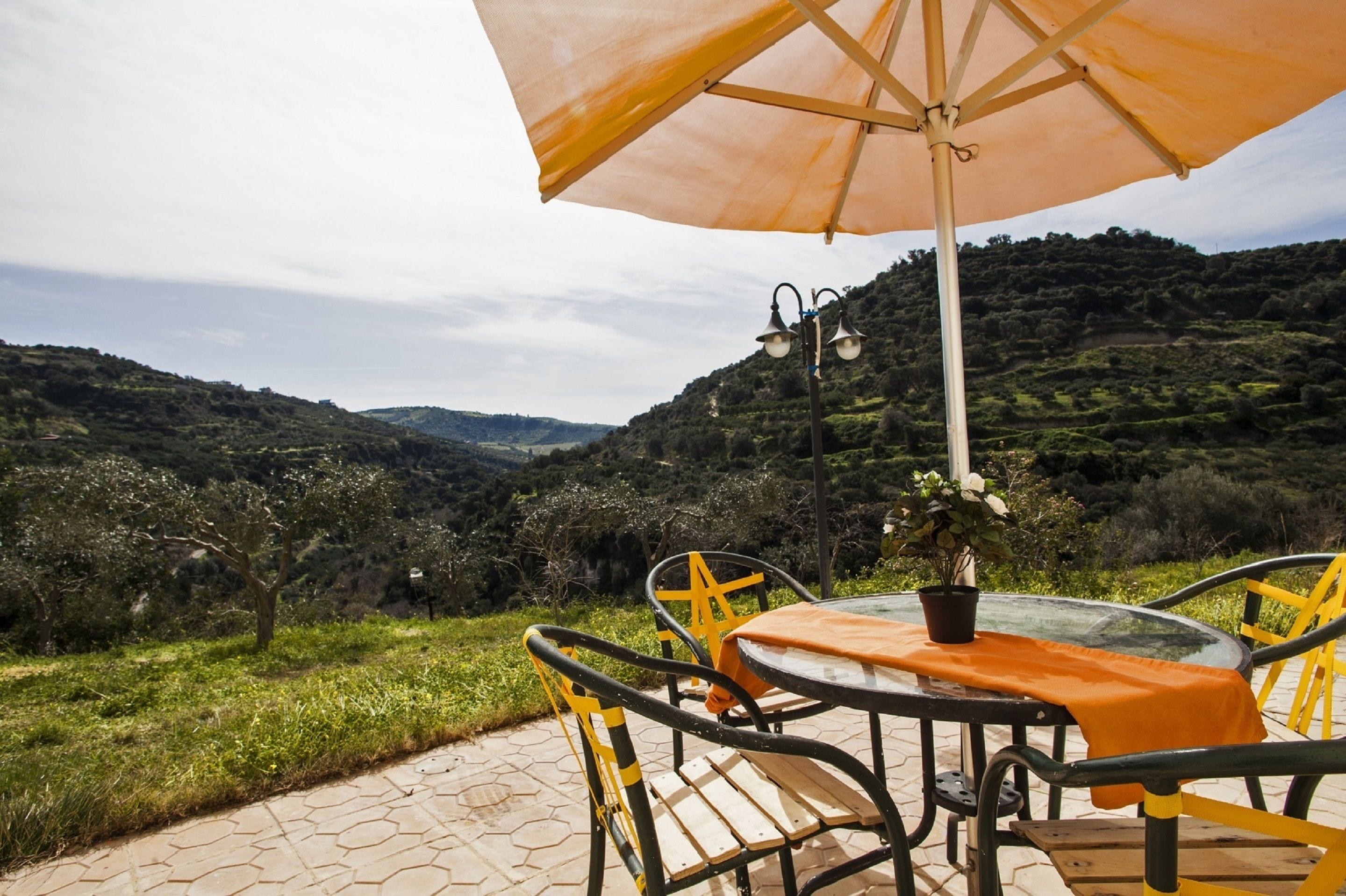 A table and chairs set outdoors with a view of a hilly landscape.