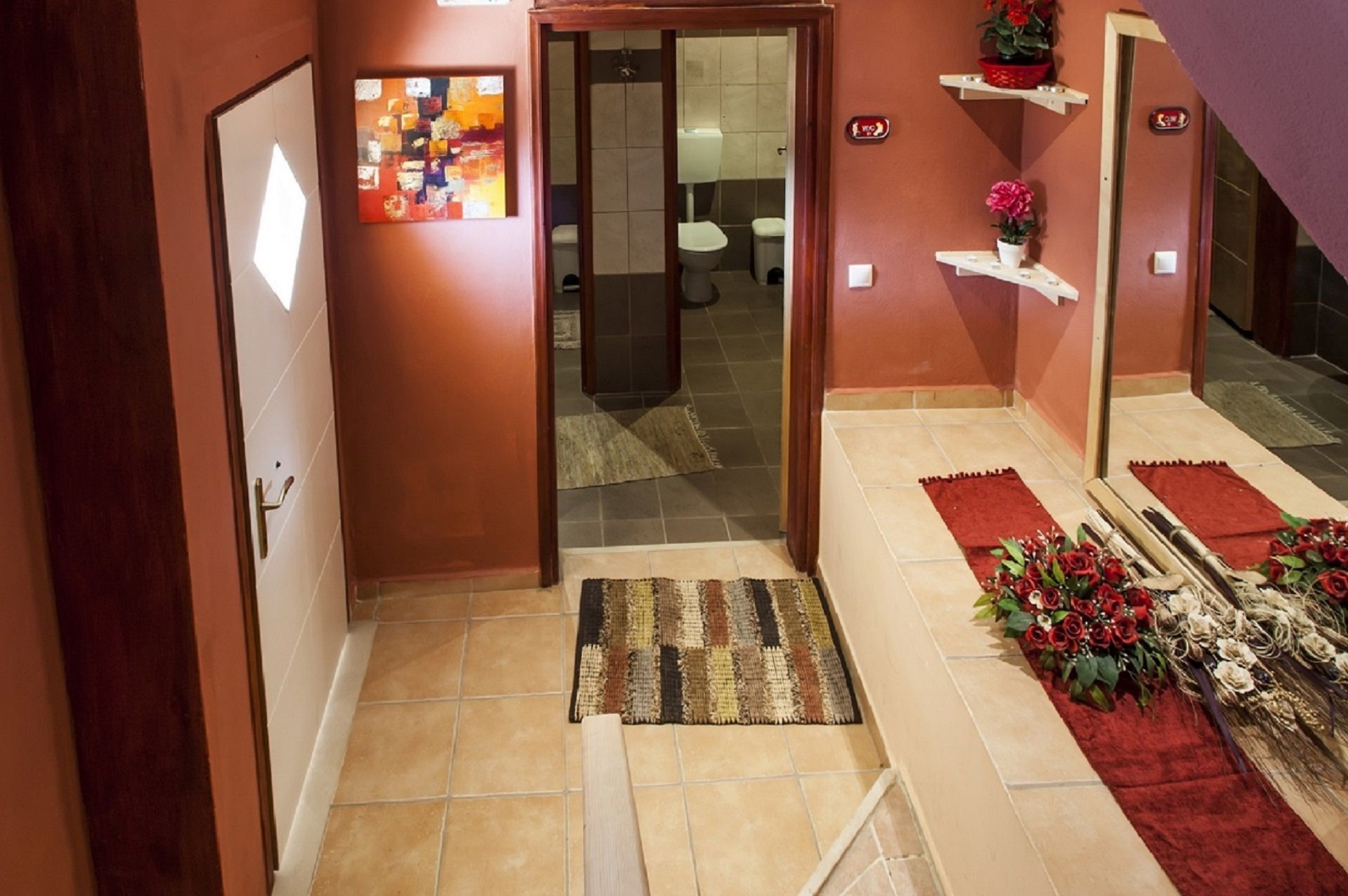 Un couloir avec une porte en bois, un sol carrelé, un tapis et une moquette rouge menant à une salle de bain.