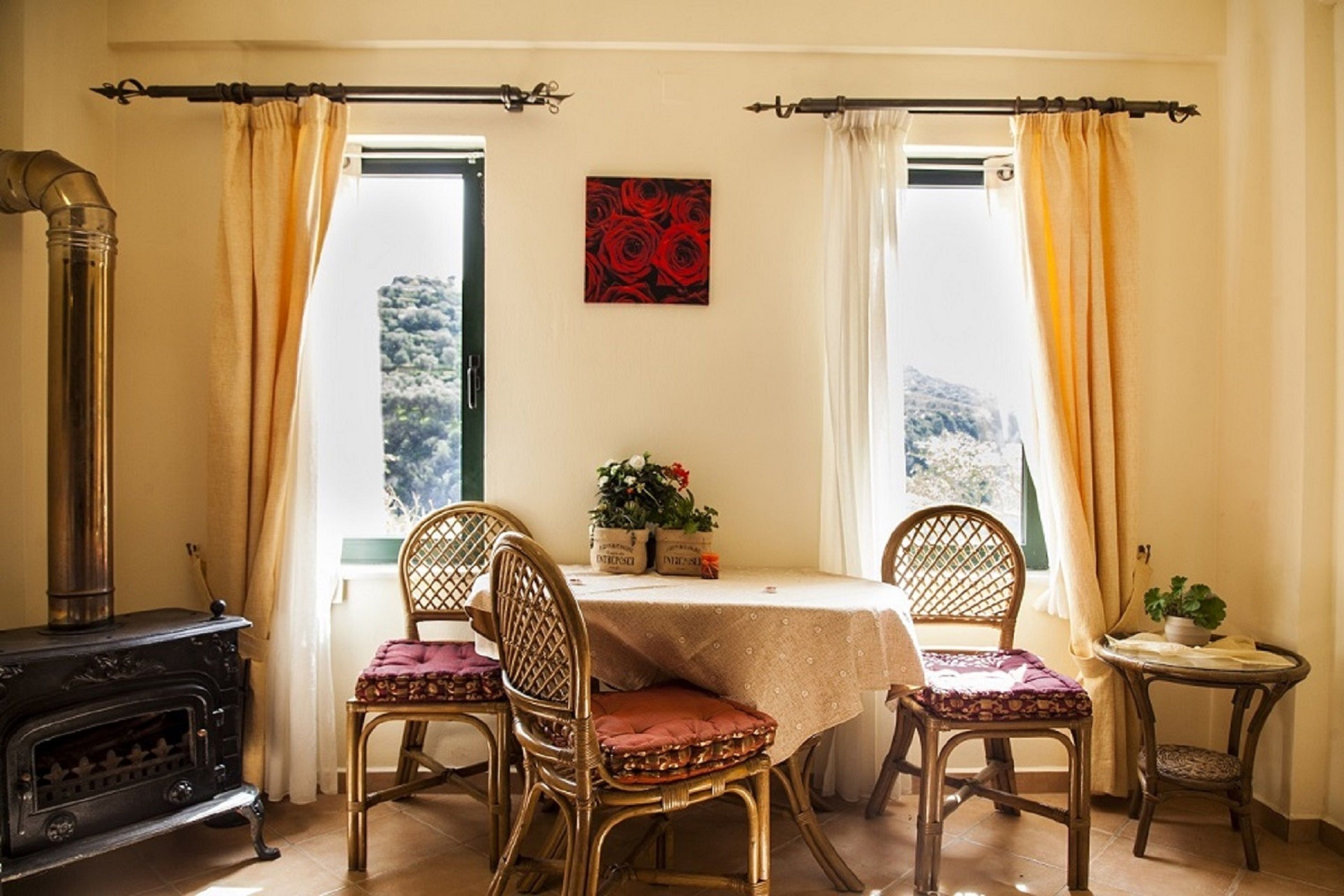 A cozy dining area with a table set for two, surrounded by wicker chairs, a small side table, and a decorative plant.