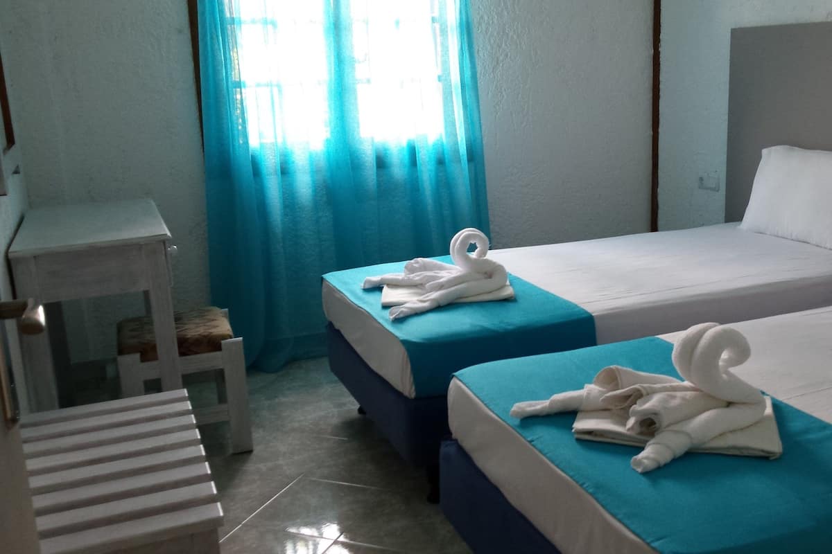 A hotel room with two beds, each with a blue bedspread and white pillows, and a white desk with a chair.