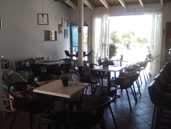 A dining area with tables and chairs, a counter, and a view of the outside. - Valentina apartments (Hersonissos)