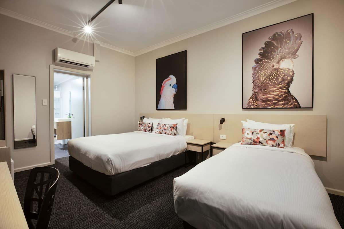 A hotel room with two beds, a large mirror, an air conditioning unit, and a painting of a rooster.