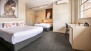 Een hotelkamer met twee bedden, een bureau en een stoel. Er hangen twee schilderijen aan de muur, en er is een raam en een airconditioning.