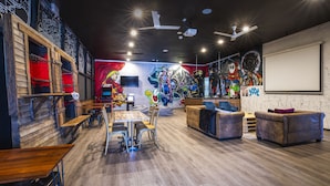 Een moderne lounge met houten tafels, comfortabele zitplaatsen, een groot muurschildering en een projectiescherm.