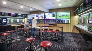 Een moderne bar met verschillende schermen waarop sport en nieuws te zien is, barstoelen en een toog.