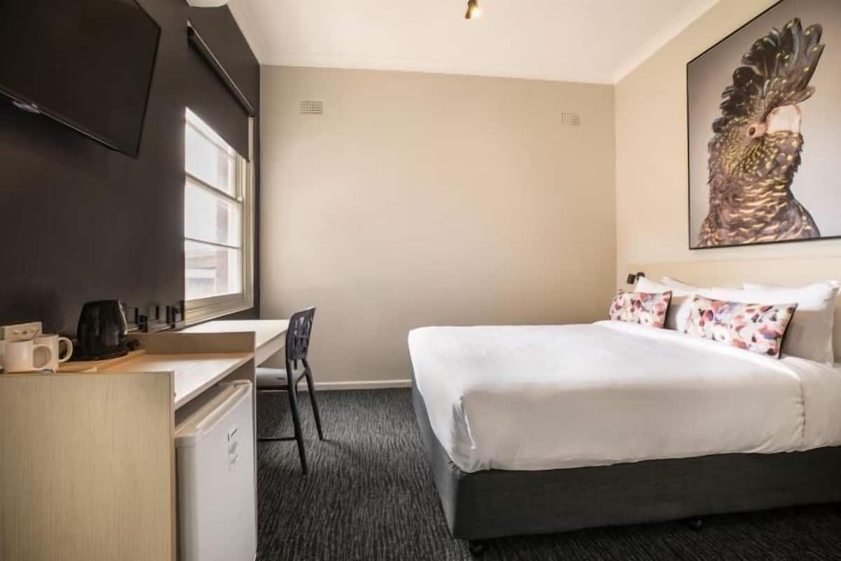 A hotel room with a bed, a desk, a chair, a television, and a painting on the wall.
