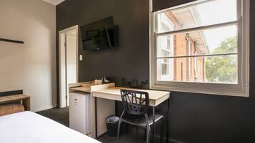 Habitación de hotel con cama, escritorio, silla, televisor montado en la pared y ventana con vistas a edificios.
