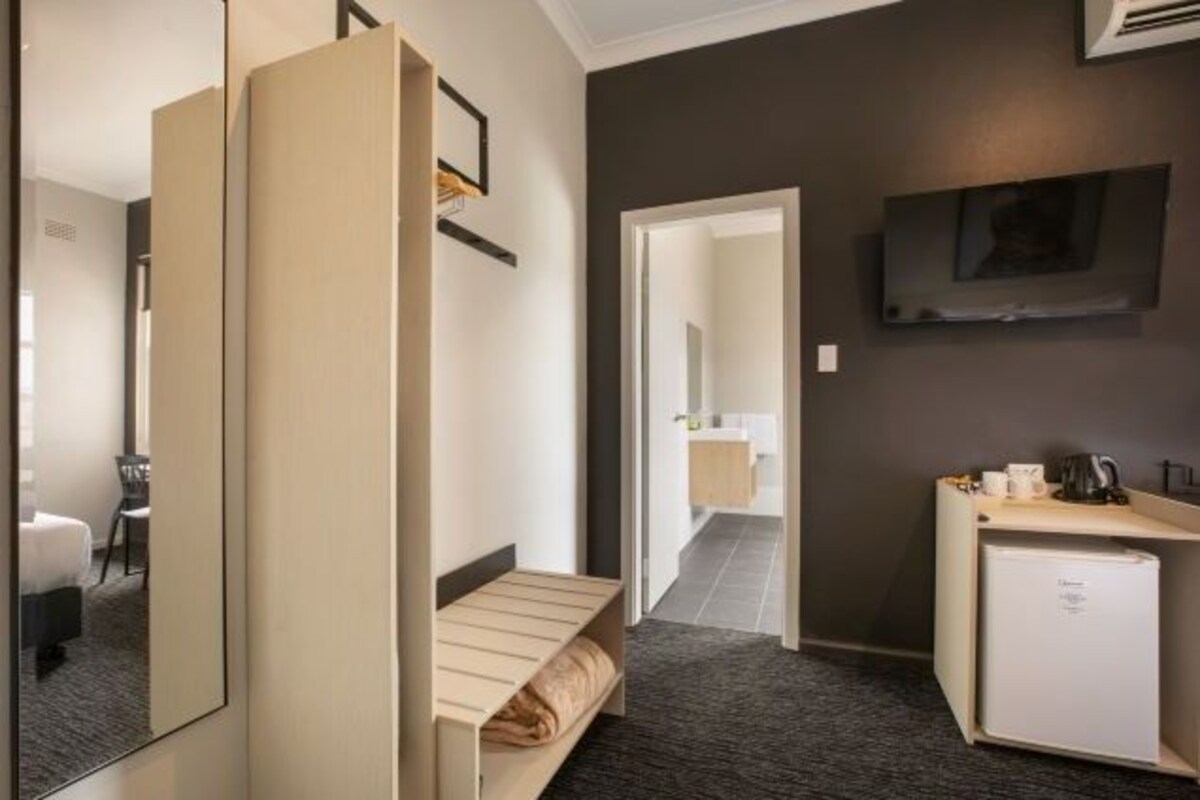 Ett hotellrum med en säng, ett litet skrivbord med ett kylskåp, en spegel och en tv på väggen.