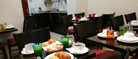 A dining area with tables set for breakfast, including croissants, bread, and beverages.