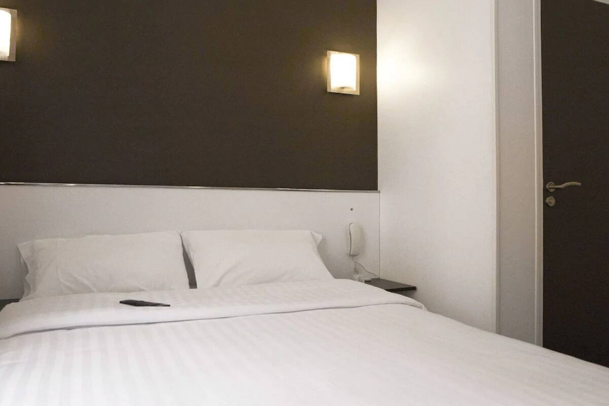 Habitación de hotel con una cama grande, dos mesitas de noche, un teléfono y dos lámparas de pared.