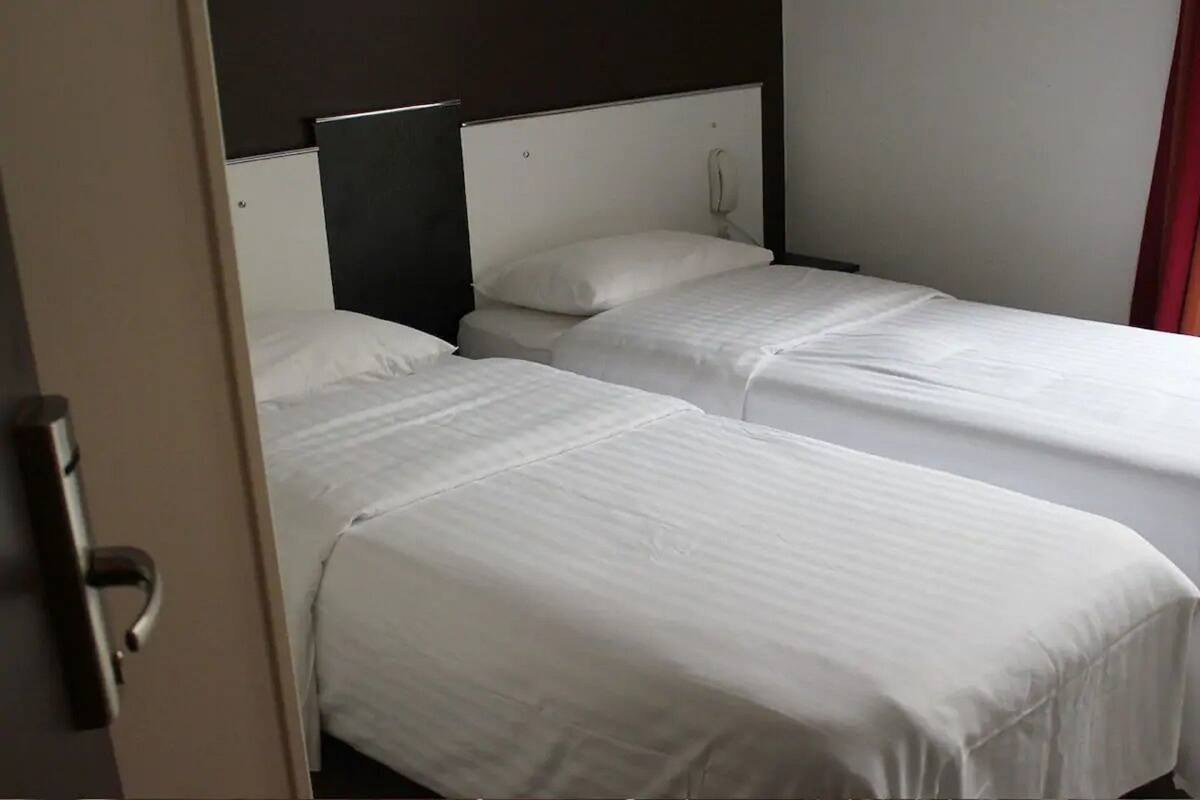 Habitación de hotel con dos camas individuales, cabecera blanca, teléfono junto a la cama y una puerta con picaporte.