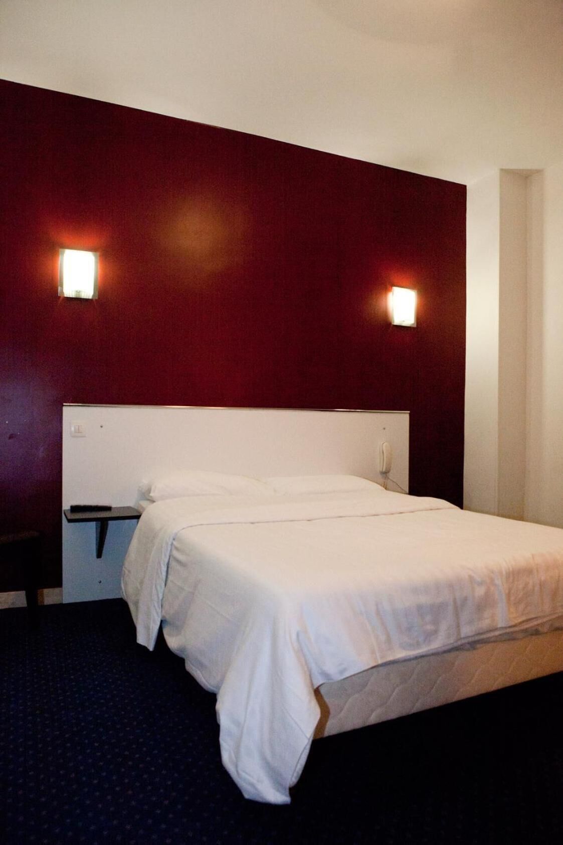 A hotel room with a single bed, a nightstand, and two wall-mounted lights.