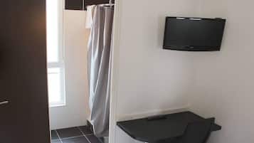 A small room with a shower curtain, a flat-screen TV mounted on the wall, and a small table with a chair.