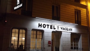 Un hotel chiamato "HOTEL WAGRAM" con una facciata classica, ampie finestre e una segnaletica che indica che è un hotel reale.
