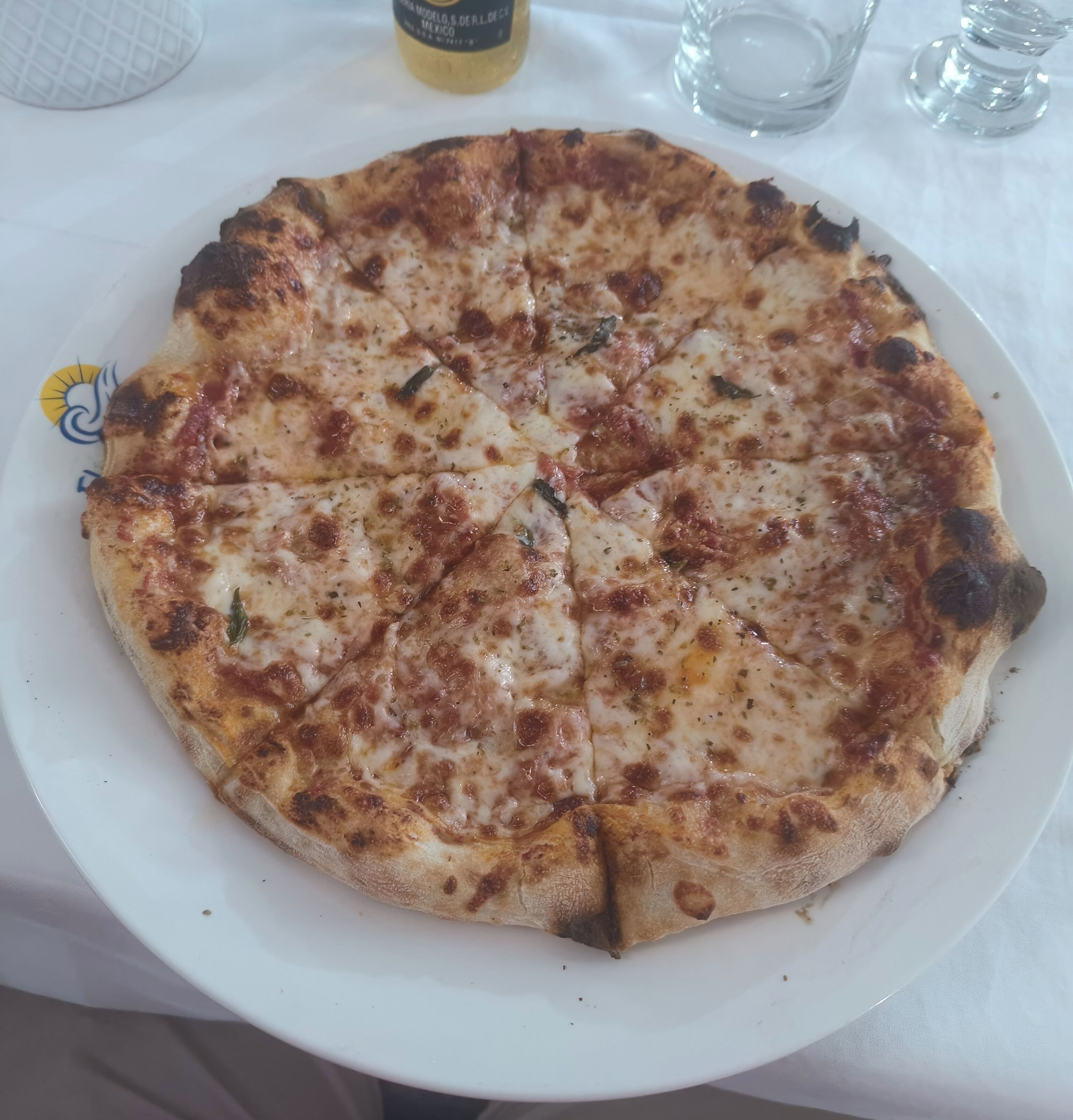 A pizza on a white plate with a sun design, placed on a table with a white tablecloth.