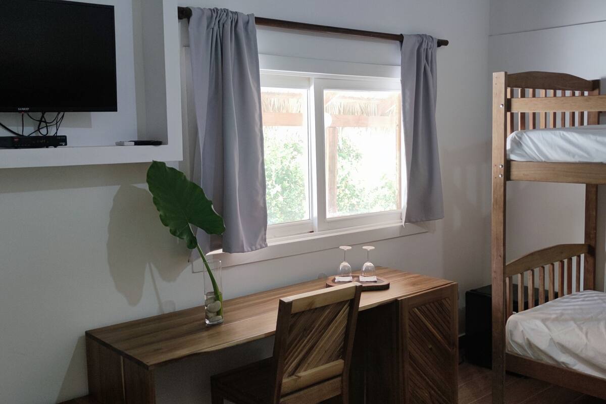 Une chambre avec un lit superposé, un bureau avec un ordinateur, une télévision et une fenêtre avec des rideaux.