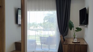 Une pièce moderne avec un banc en bois, une petite table sur laquelle est posé un vase, et un téléviseur fixé au mur. Un grand miroir se trouve à gauche, et on peut voir, à travers la fenêtre, un espace extérieur avec un banc et une table.