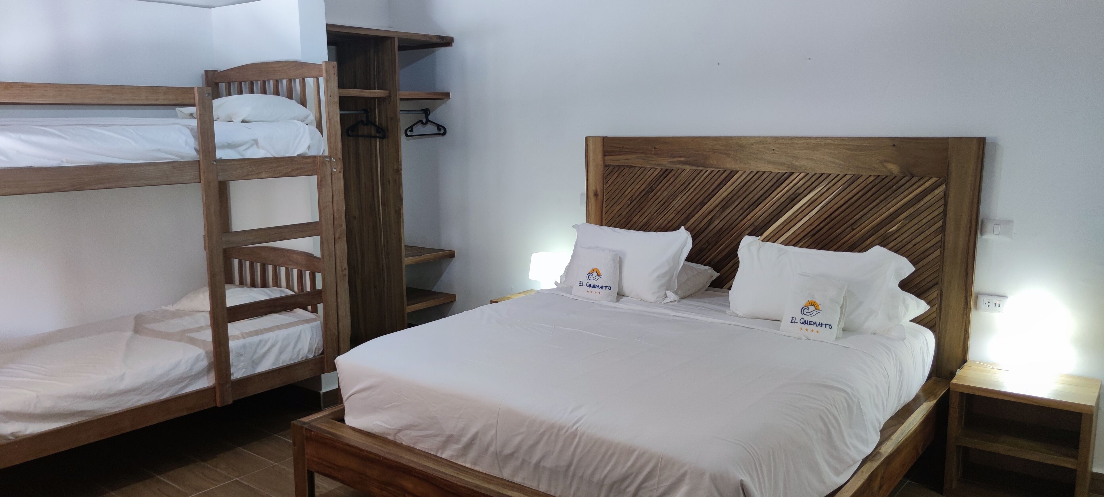 A room with a single bed, a bunk bed, wooden headboard, and a bedside table.