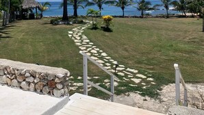 Un sentier menant à une plage bordée de palmiers et surmontée d’une structure au toit de chaume.