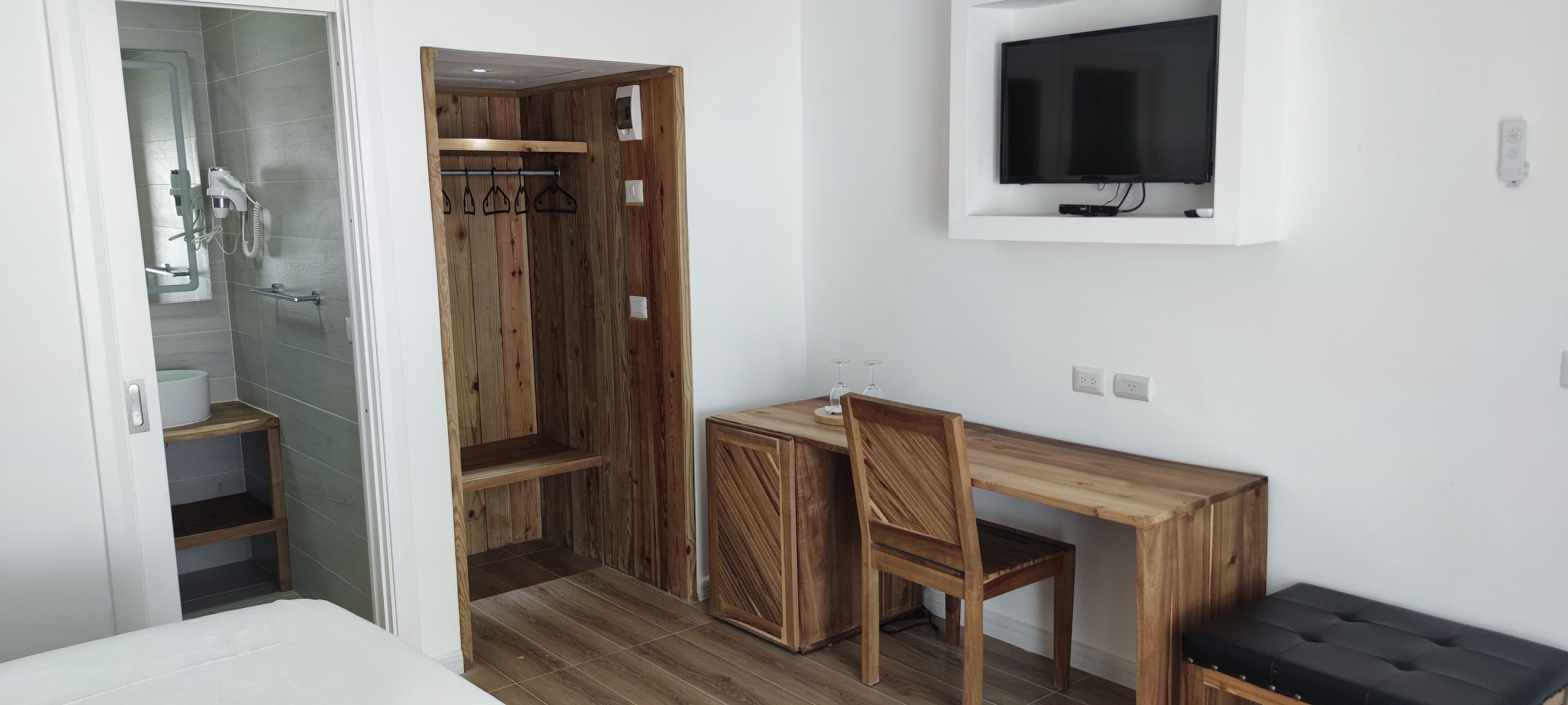A compact room with a wooden desk, chair, and a TV mounted on the wall.