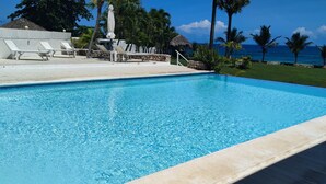 Une piscine d’un bleu éclatant, bordée de chaises longues blanches, avec vue sur l’océan.