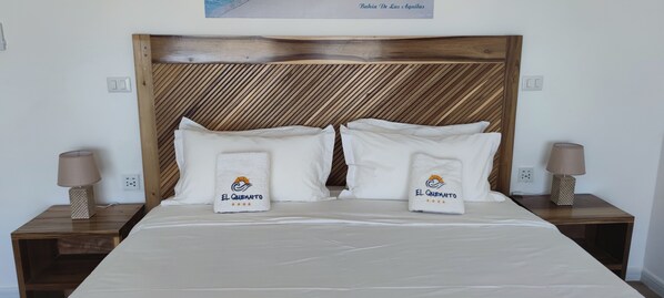 Una cama bien hecha con dos almohadas y dos toallas, cada una con el logotipo "El Quenamo".
