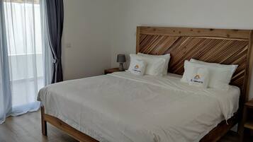 A neatly made bed with a wooden headboard, two bedside tables with lamps, and a window with sheer curtains.