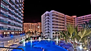 A nighttime view of a hotel with a large swimming pool, multiple balconies, and palm trees. - Royal Tulip City Center Tanger (Tangier)
