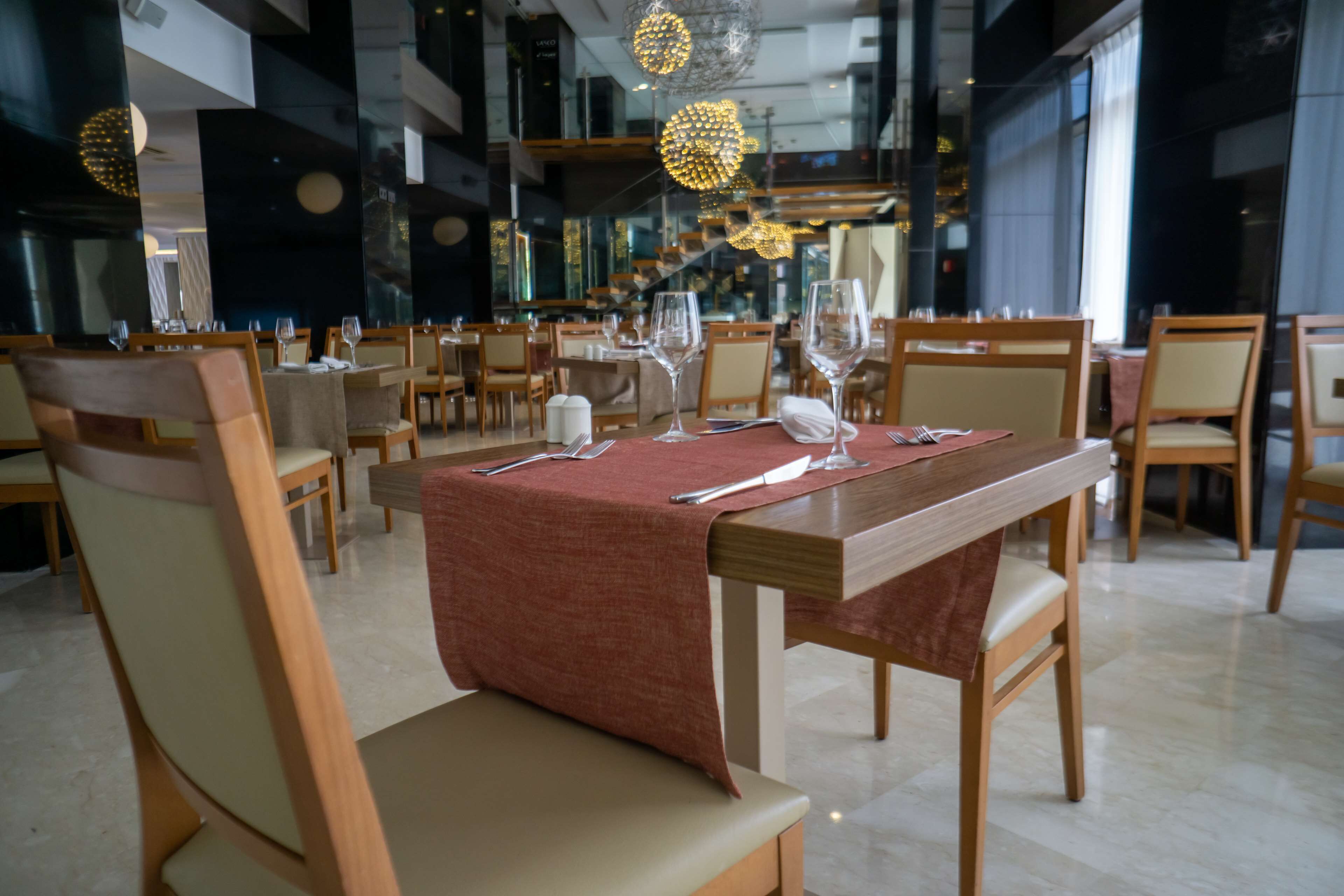 A restaurant with multiple tables set for dining, featuring wooden chairs and a red tablecloth.