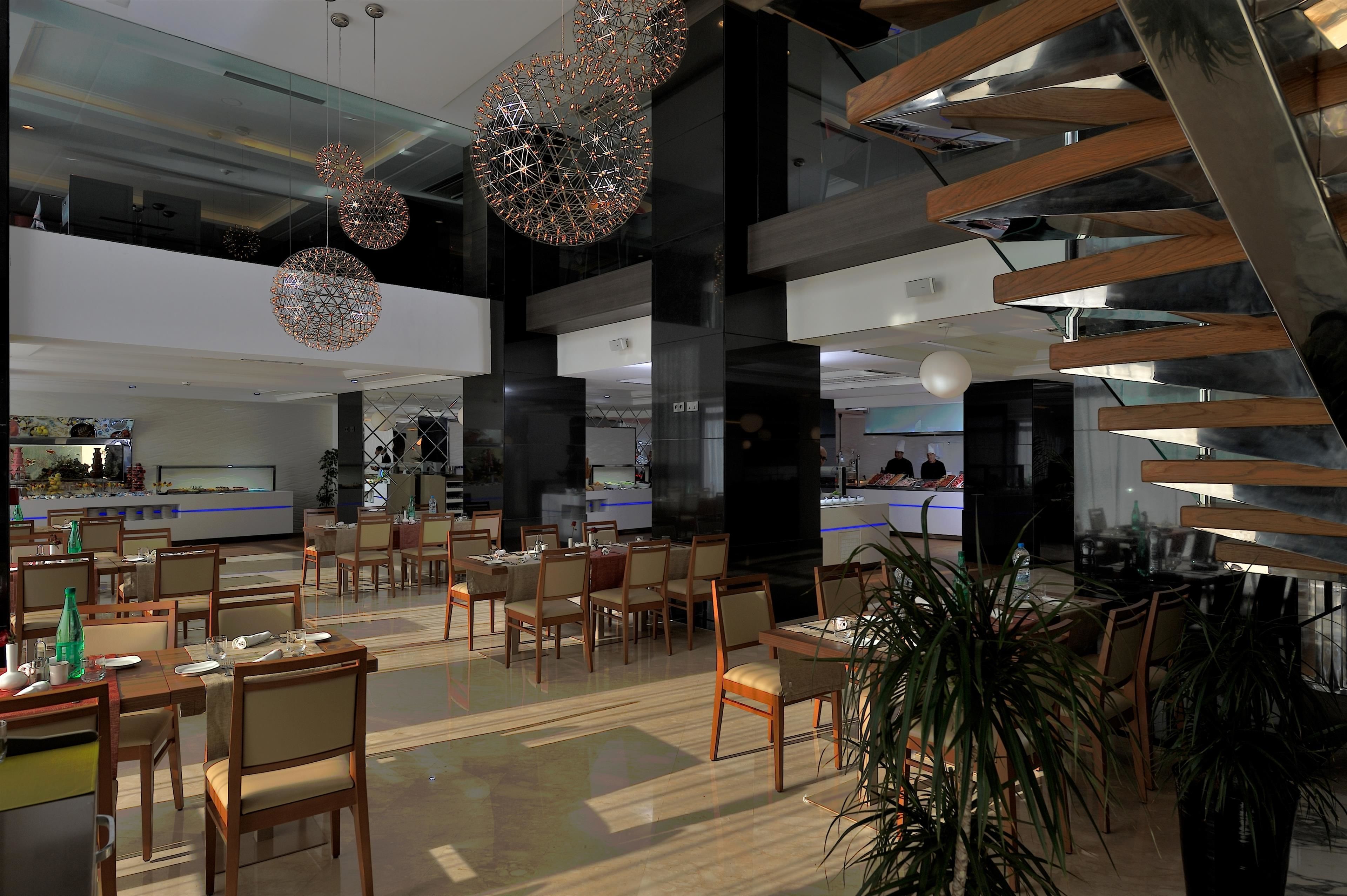 Un amplio vestíbulo de hotel con varias zonas de restauración, candelabros modernos y una escalera.