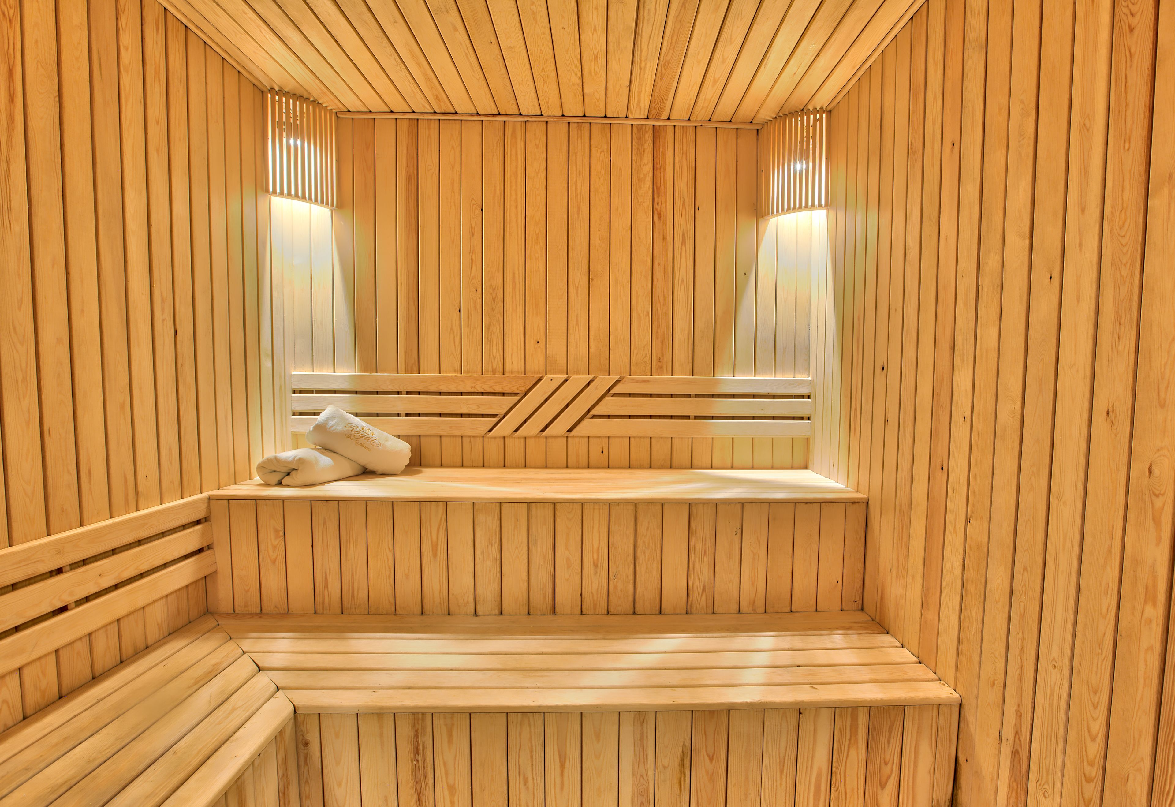 A sauna with wooden walls and benches, a bench with a towel, and two wall-mounted lights.