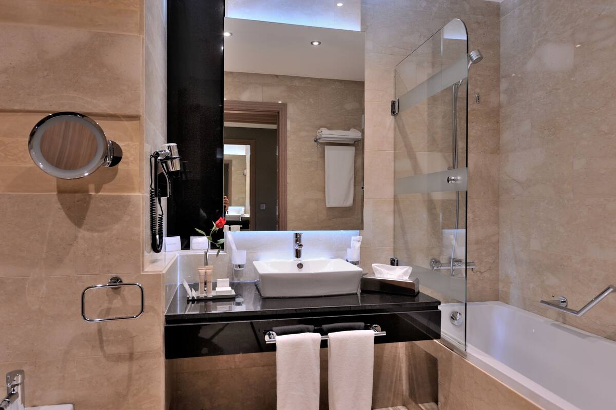 Un baño moderno con un espejo grande, un lavabo, una bañera y una ducha con mampara de cristal.