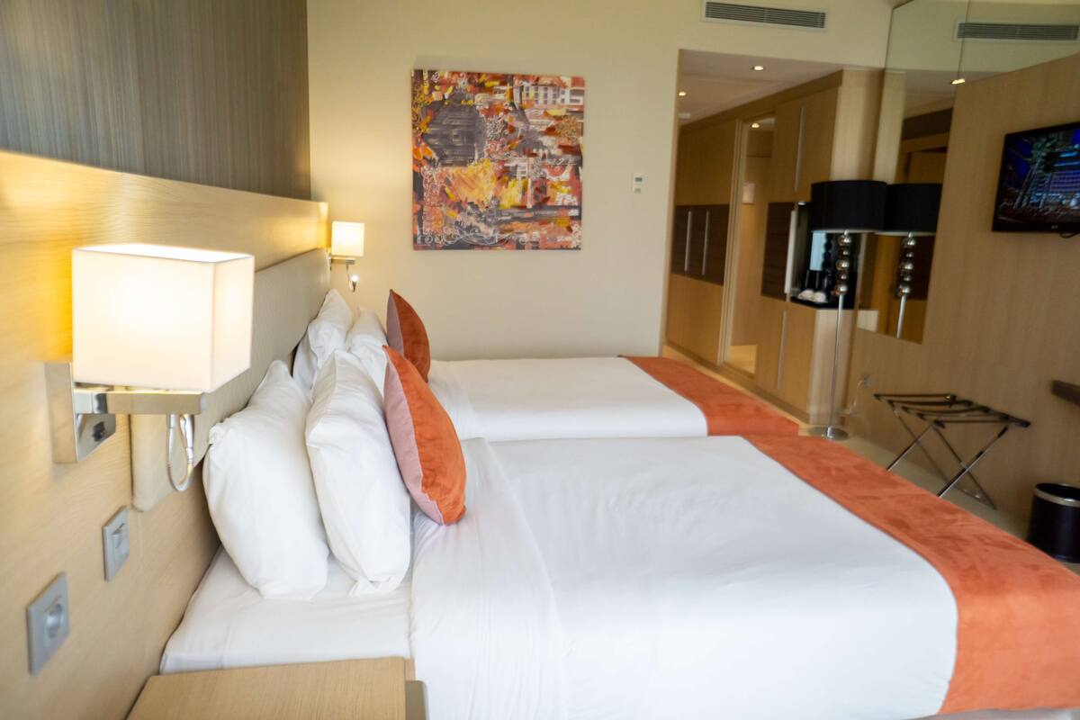 Una habitación de hotel con dos camas, un televisor montado en la pared y un cuadro.