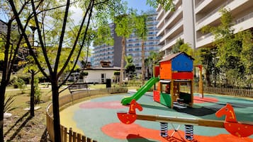 Children can play on the seesaw, slide, and climbing structure in this playground area surrounded by trees and shrubs.
