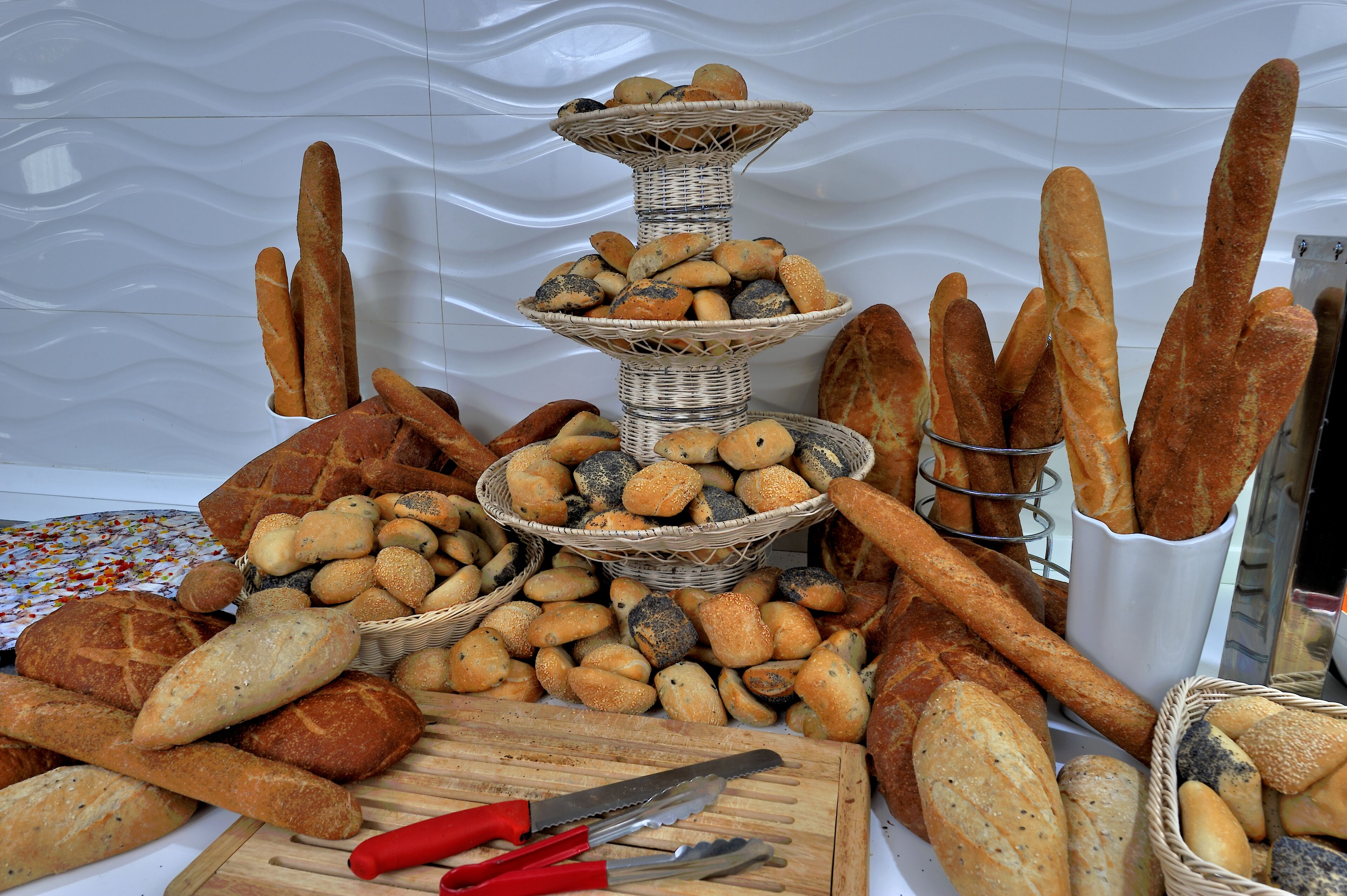 A variety of breads and loaves displayed on a table with a cutting board and utensils.
