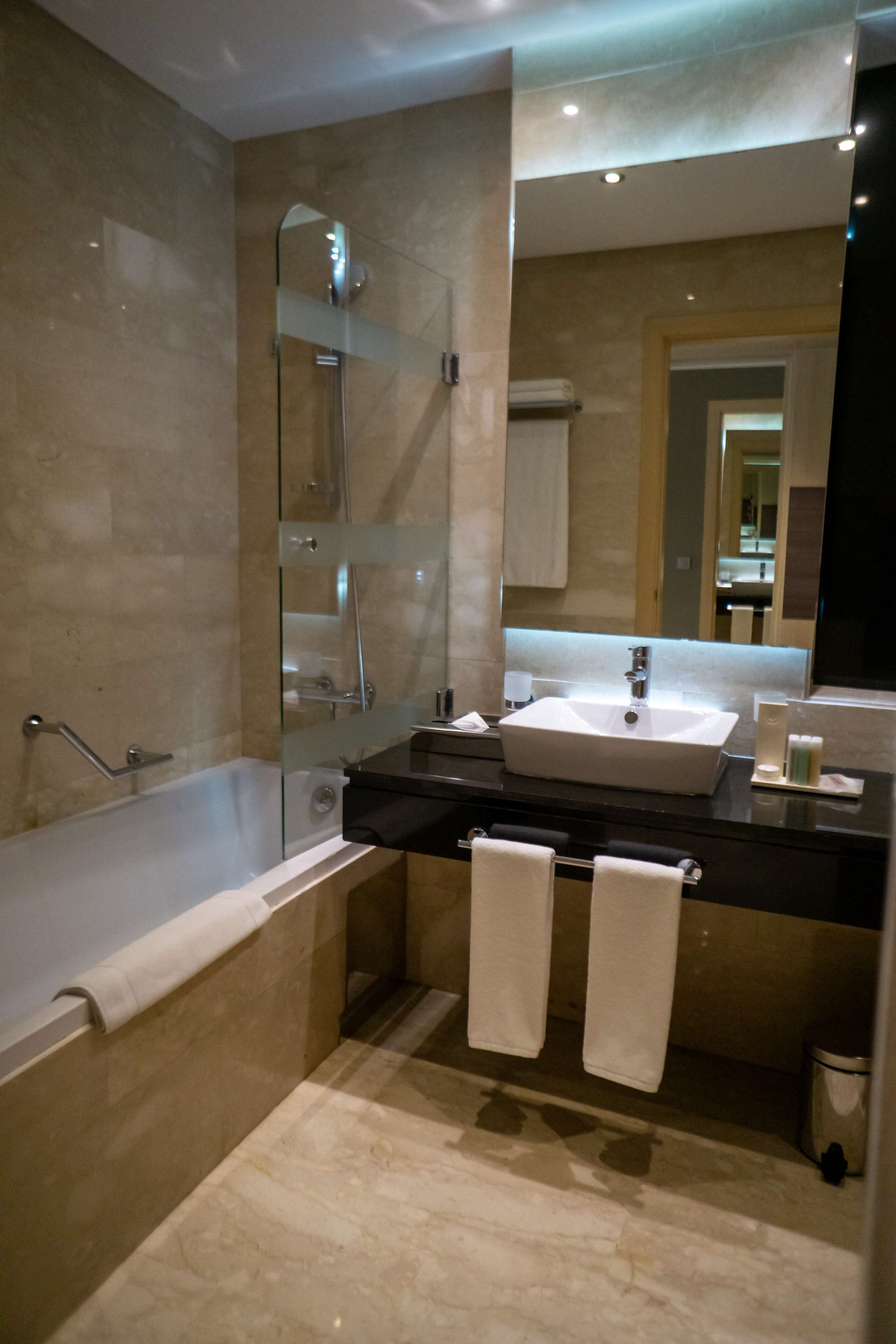 Une salle de bain moderne avec une douche à parois de verre, un grand lavabo et deux serviettes posées sur le comptoir.