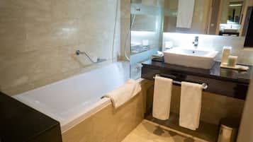 A modern bathroom with a bathtub, a sink, and a mirror. There are towels hanging on the wall and a trash can.