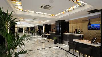 A modern hotel lobby with a reception desk, seating area, and a large TV screen.