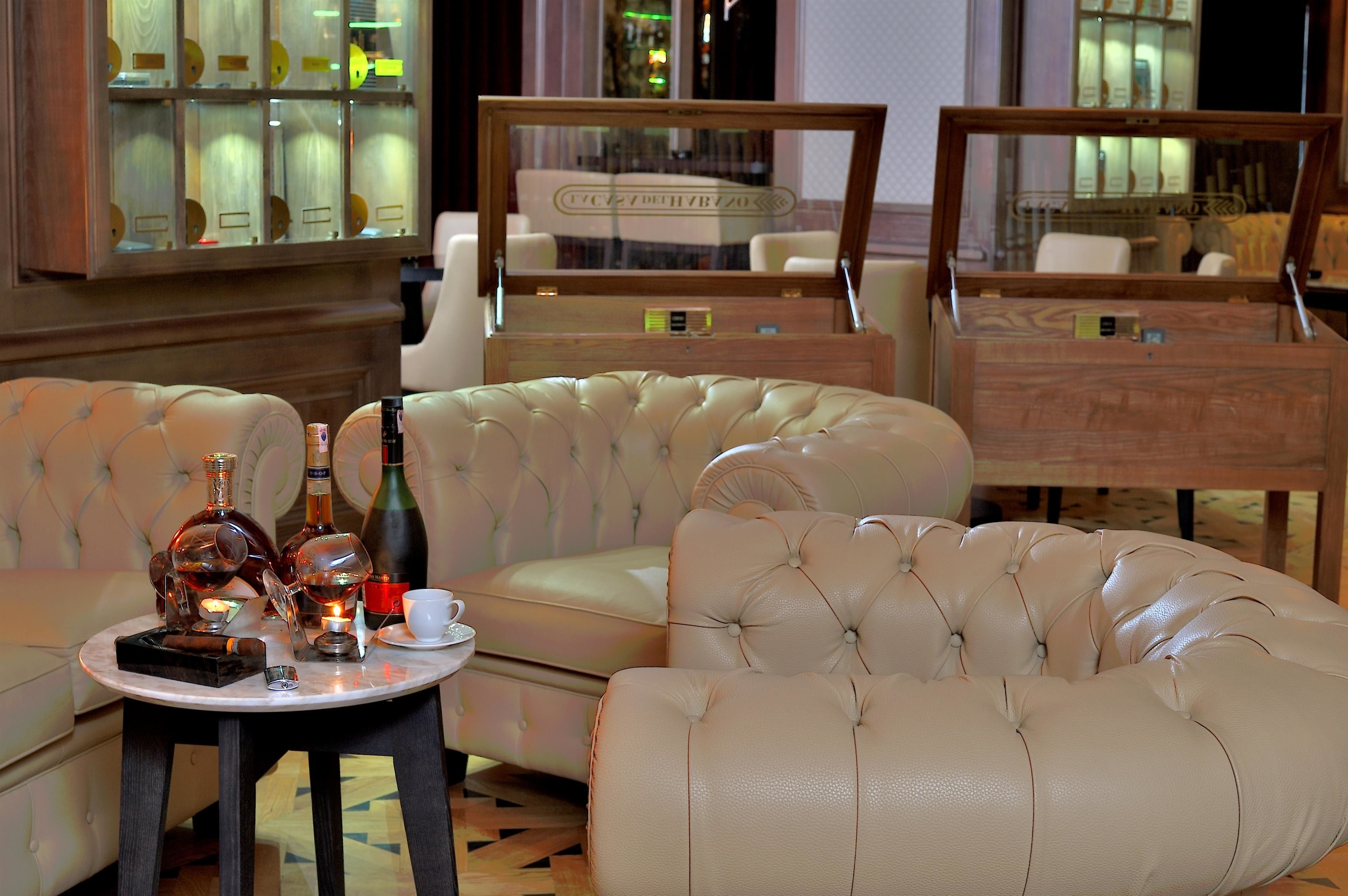 A luxurious room with a tufted sofa, a small table with bottles and glasses, and a large mirror.