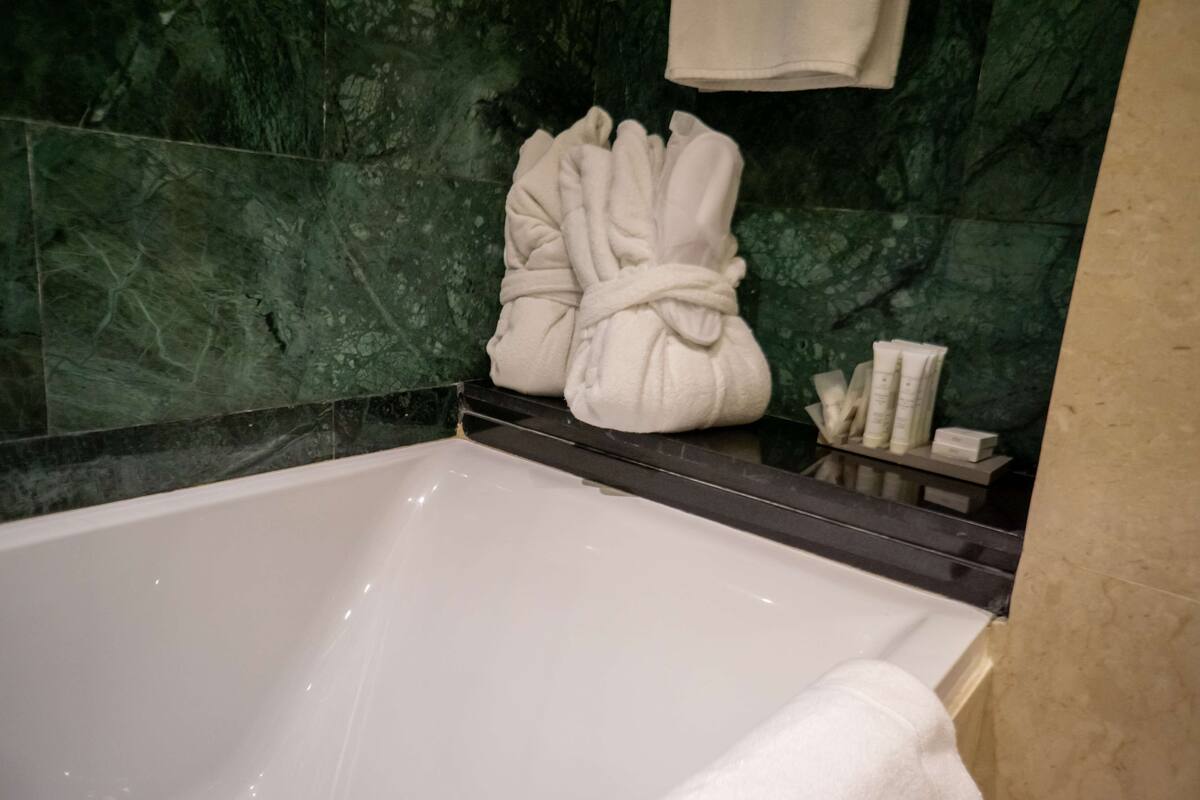 Un baño con bañera, paredes de mármol verde y un perchero con toallas.