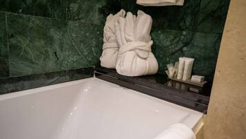 Une salle de bain avec une baignoire, des murs en marbre vert et un porte-serviettes avec des serviettes.